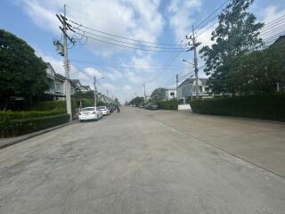 Wide residential street with lined houses and parked cars under a clear sky