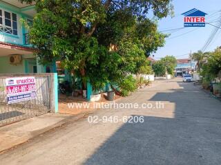 Suburban street view of a blue house with a for sale sign and lush greenery