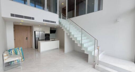 Modern open-plan living space with glass staircase and sleek kitchen