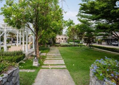 Lush green garden with pathway and trees in front of a residential property