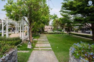 Lush green garden with pathway and trees in front of a residential property