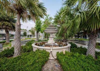 Elegant garden in a residential area with a central fountain surrounded by lush greenery and palm trees