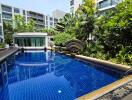 Blue swimming pool in a luxurious apartment complex with lush garden and modern amenities