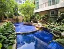 Lush garden with a small blue-tiled pool surrounded by tropical plants near a building