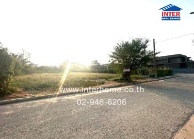 Sunlit exterior view of vacant land with residential potential, advertising real estate agency contact information