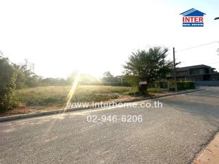 Sunlit exterior view of vacant land with residential potential, advertising real estate agency contact information