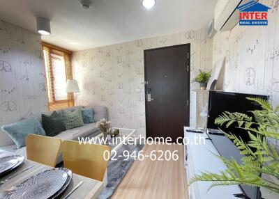 A cozy living room with a sofa, wooden table, and a TV stand. There is a door, window, indoor plants, and decorative wallpaper with a geometric pattern.