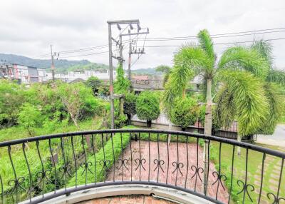 View from balcony overlooking a lush garden with palm trees and urban landscape