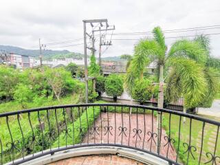 View from balcony overlooking a lush garden with palm trees and urban landscape