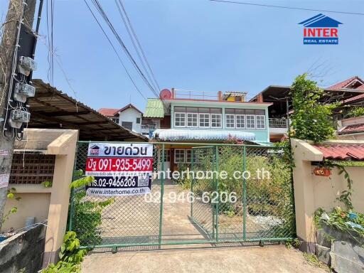 Exterior view of a two-story residential building with a gate and for sale signs