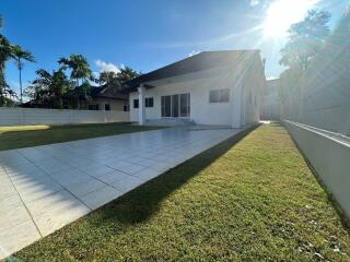 Sunny exterior view of a modern single-story house with spacious tiled patio and well-maintained lawn