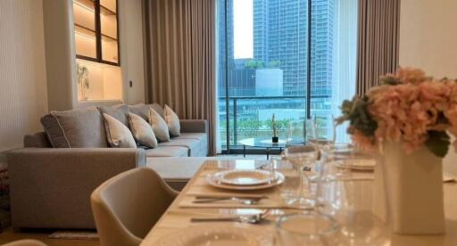 Modern living room with view of cityscape through large windows, featuring a comfortable sofa and elegant dining area