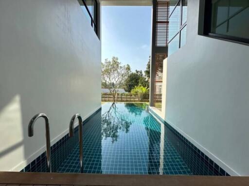 Private outdoor swimming pool with blue tiles and steel ladder, bordered by modern white building walls under clear skies