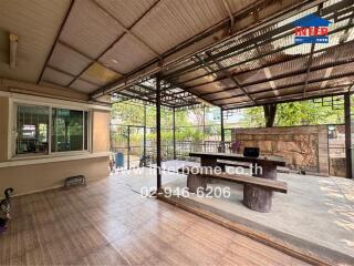 Spacious covered patio area with wooden furniture and surrounding garden