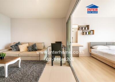 Modern bedroom with an open sliding glass door leading to a balcony, featuring a neatly made bed and a comfortable seating area