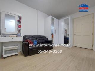 Spacious living room with black leather sofa, white walls, and laminate flooring