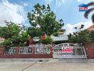 Exterior view of a residential house with gate and lush greenery