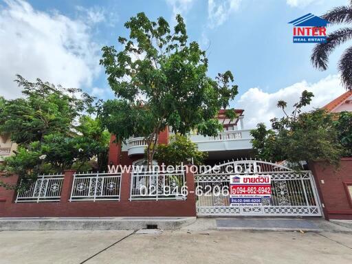 Exterior view of a residential house with gate and lush greenery