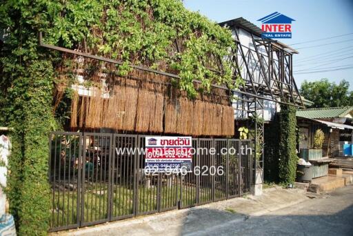 lush greenery covering a rustic house exterior with real estate signage