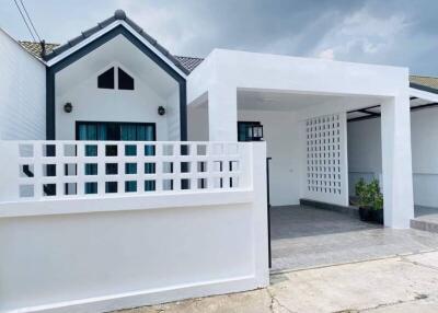 Modern white residential building exterior with a covered entrance and privacy fence