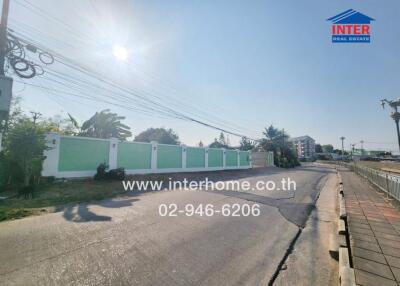 Sunlit street view with green fence and clear sky