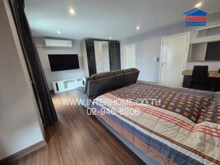 Modern bedroom with large bed, wall-mounted TV, and wooden flooring