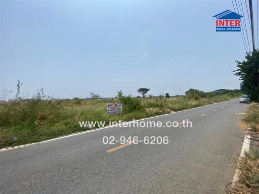 Empty plot of land available for sale along a roadside with clear signage