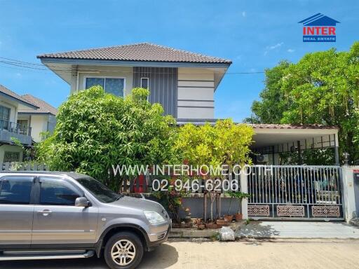 Two-story residential house with surrounding greenery and a parked car