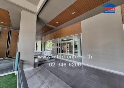 Modern building entrance with a spacious covered walkway, wooden ceiling panels, and tiled flooring