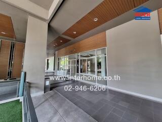 Modern building entrance with a spacious covered walkway, wooden ceiling panels, and tiled flooring