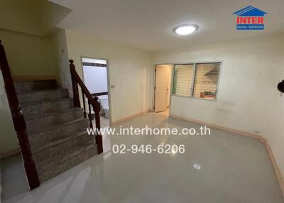 Interior view of a living area with stairs leading to the second floor, a doorway to another room, and a window.