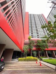 Modern high-rise residential building with a vibrant red facade and lush green landscaping