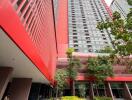 Modern high-rise residential building with a vibrant red facade and lush green landscaping