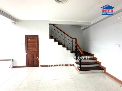 Spacious living area with white tiles and a wooden staircase