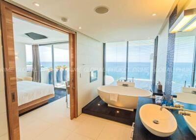 Luxurious bathroom with freestanding tub and view into bedroom with ocean view