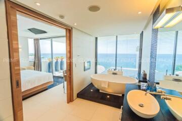 Luxurious bathroom with freestanding tub and view into bedroom with ocean view