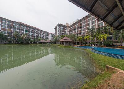 Exterior view of a residential building complex with a large swimming pool and surrounding greenery