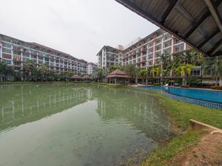 Exterior view of a residential building complex with a large swimming pool and surrounding greenery