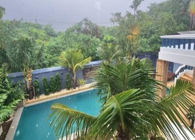 Tropical outdoor pool area with lush greenery and rainy weather