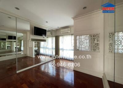 Spacious living room with wooden flooring, large mirrors, and modern wall-mounted TV