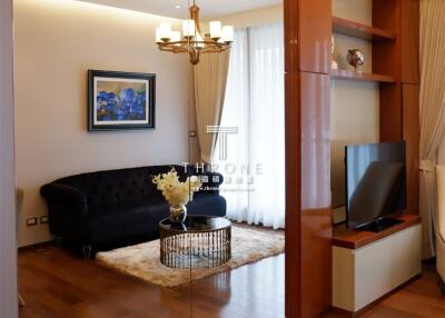 Modern living room with hardwood floors, a cozy black couch, a TV, a chandelier, and a large mirror wall