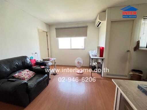 Living room with a black leather sofa, small desk, and air conditioning unit