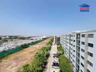 View of a residential building complex with parking area and open land in the vicinity