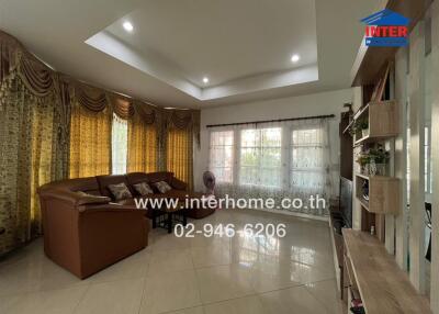 Spacious living room with brown sofa, large windows with drapes, tiled floor, and built-in shelving.