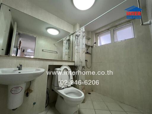 Clean and modern bathroom with tiled walls and floors, featuring a sink, toilet, and shower area with curtain.