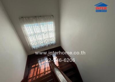 Staircase with wooden rails and a window with lace curtains