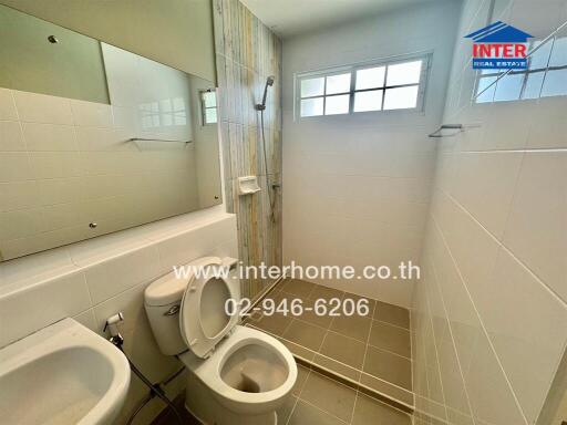 Bathroom with toilet, sink, shower area, and tiled walls