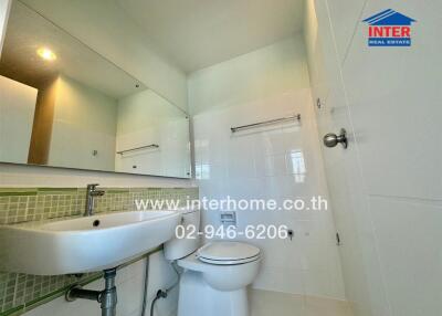 A clean and modern bathroom with white tiled walls, a large mirror, a sink, and a toilet.