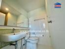 A clean and modern bathroom with white tiled walls, a large mirror, a sink, and a toilet.