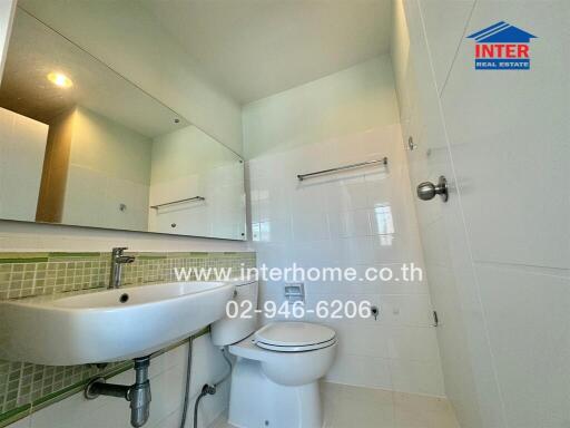 A clean and modern bathroom with white tiled walls, a large mirror, a sink, and a toilet.